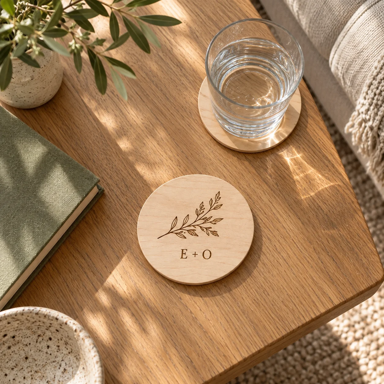 An overhead view of engraved wooden coasters beside a water glass and olive book
