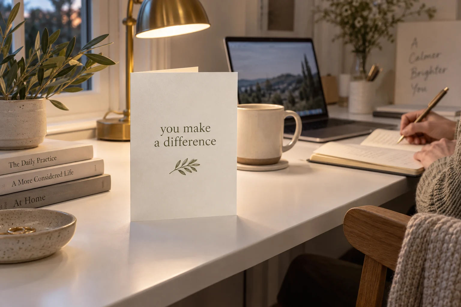 A large you-make-a-difference card beside a laptop and someone writing at a white desk in early evening