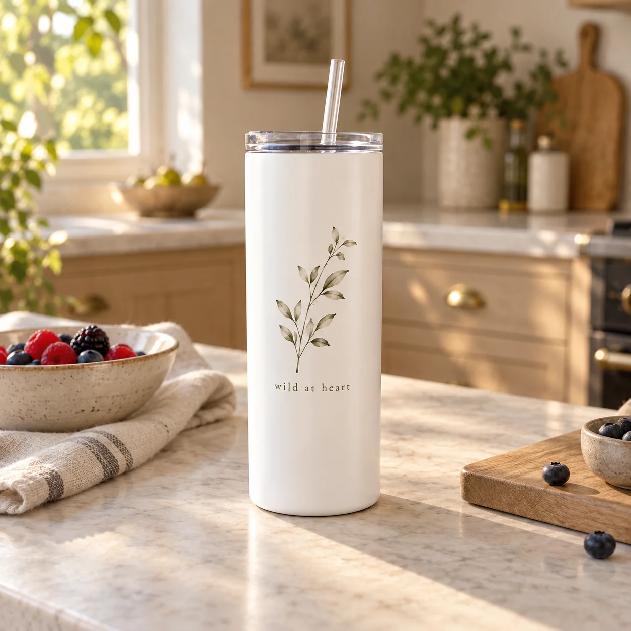 A white botanical skinny tumbler on a pale kitchen counter beside berries and linen