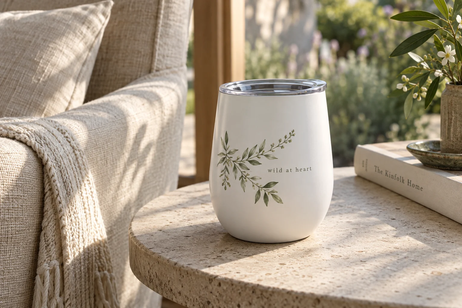 A botanical stemless tumbler on a stone side table beside a linen chair